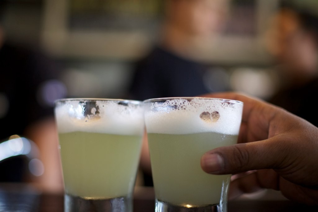 What are you waiting for? Grab the other glass and say, Salud! Visit Peru Image: A hand reaches for one of two Pisco sours on a table.