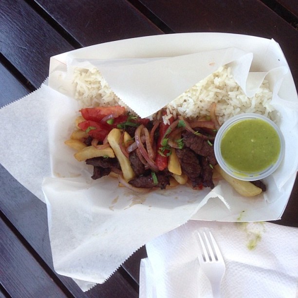 Bet that green sauce on the side is tasty too. Visit Peru Image: A to-go basket is filled with the colourful beef and vegetable stir-fry has fluffy white rice on the side, and fried potatoes throughout. A green dipping sauce sits in the basket, and a napkin and white plastic fork are off to the side.