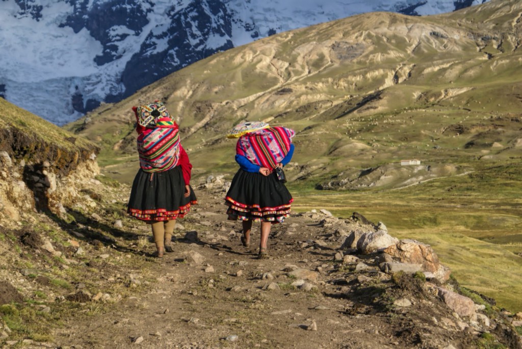 It's hard to imagine the Andes being a part of your daily life... Central and South American Ruins Image: Two women have their backs to us. They are wearing colourful skirts, and are carrying equally colourful bundles on their backs as they walk down an incline in the Andes.