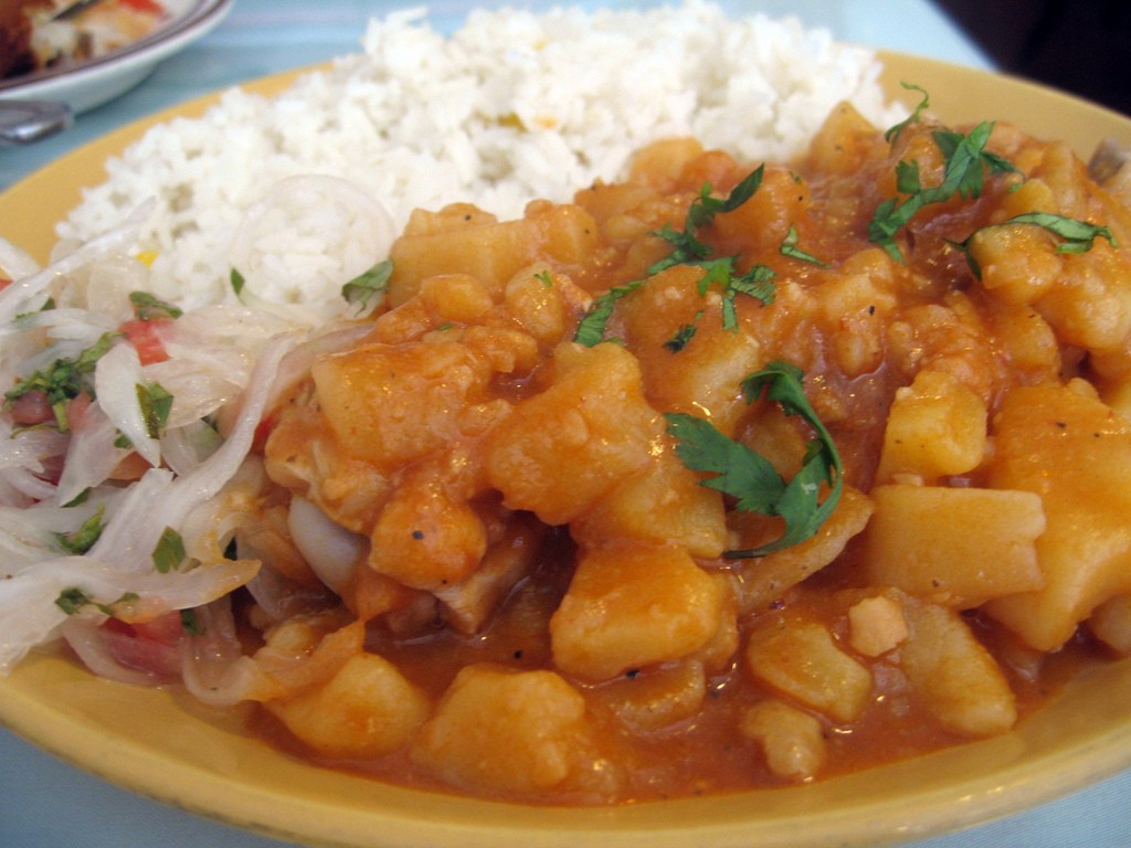 Who knew a plate of food could be described as 'warm and inviting?' Visit Peru Image: The hearty potato stew described in this section of our Peru food tour is heaped onto a yellow plate, and accompanied by white rice, and what appears to be a vegetable slaw.