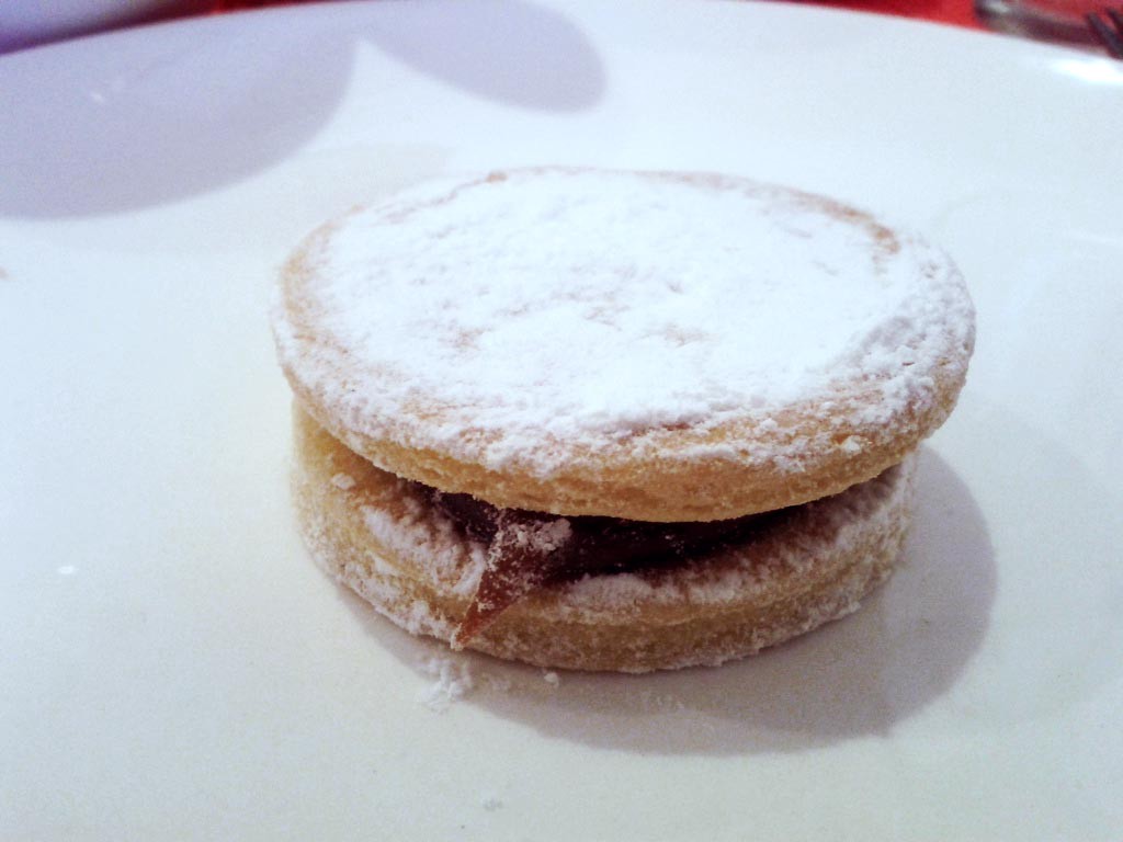 #Delicious! Visit Peru Image: A single alfajores sits on a white plate, and has been dusted with a generous amount of powdered (or confectioner's) sugar.