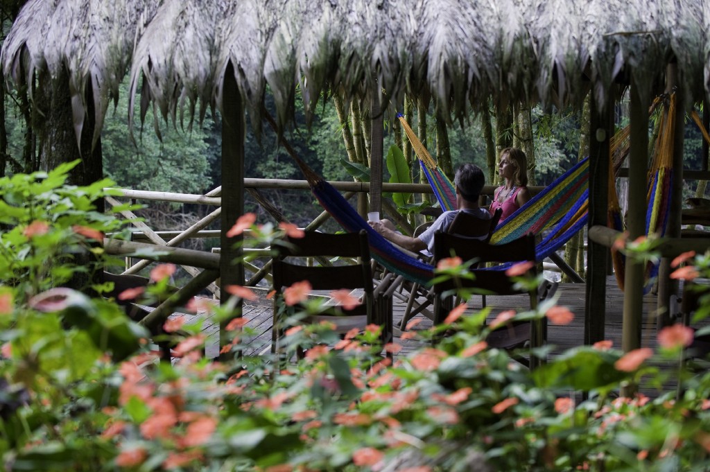 No big deal; just a couple chatting in the midst of a luscious green jungle. Eco-Friendly Costa Rica Image: A couple sits in two hammocks in an open-air structure covered by a leafy roof. They are talking and enjoying the surrounding jungle scenery.
