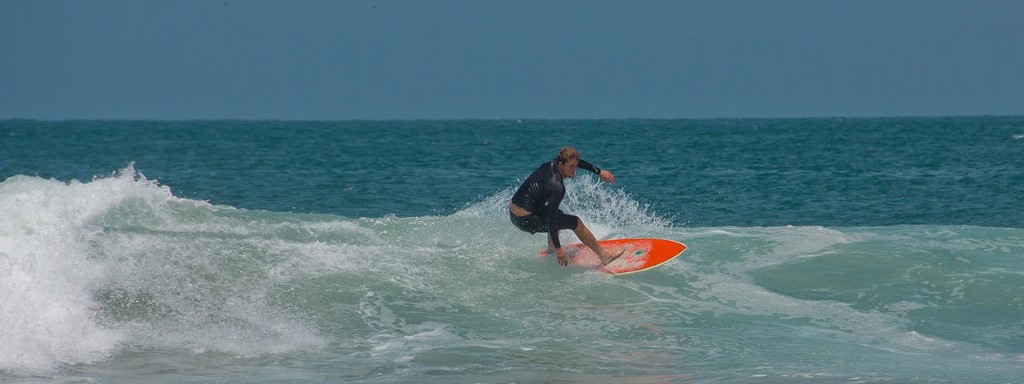 Well, someone looks like he's enjoying himself. Best Surfing Beaches: A surfer in a black two piece wetsuit rides a red surf board in the water.
