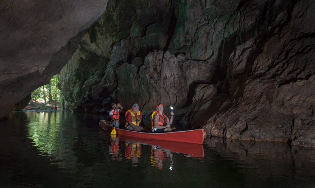 The best part about these cave floats? You're accompanied by professionals who have taken your route many times. Cave Floating Image: Three people in a canoe pass between the rocky walls of a cave.