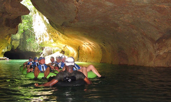 A group of cave tubers sits reclined in tubes, light from the cave opening is seen behind them.