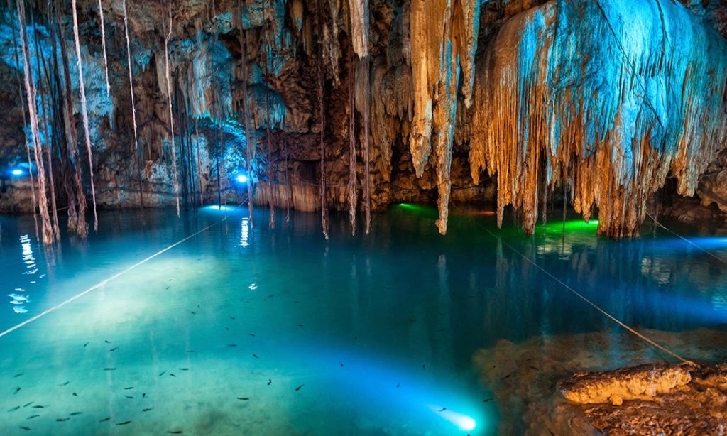 Remember—stalactites point down, stalagmites point up! Cave Floating Image: Stalactites drop down from the top of a cavern—hovering above turquoise water which is illuminated from below. Fish can be seen swimming.