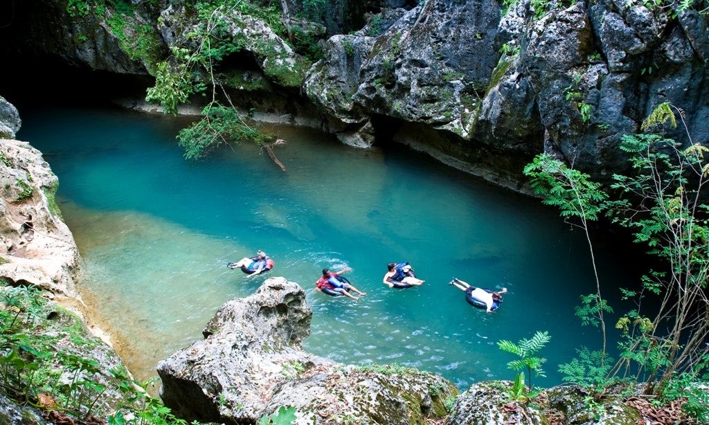 Even some of Belize's adventurous activities are laid-back! Moving to Belize Image: An aerial view of four tubers emerging from a cave and floating into a beautifully blue pool surrounded by jungle.