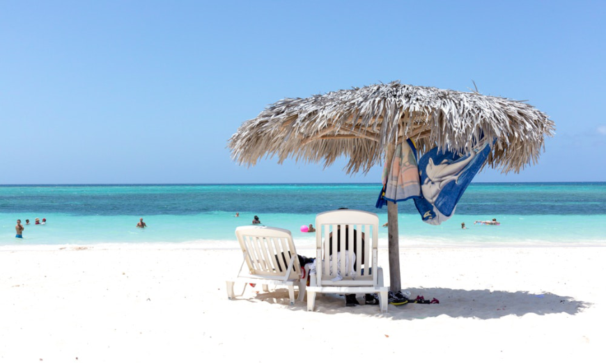 Enjoy the warmth or the shade—your vacation, your choice. Are Cuba's Beaches Nice Image: A leafy beach umbrella strewn with a towel shades two chairs on the beach.
