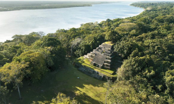 Near the river's edge waits history and wonder. Belize River Tour Image: Lamanai and a river are divided by a lush canopy.