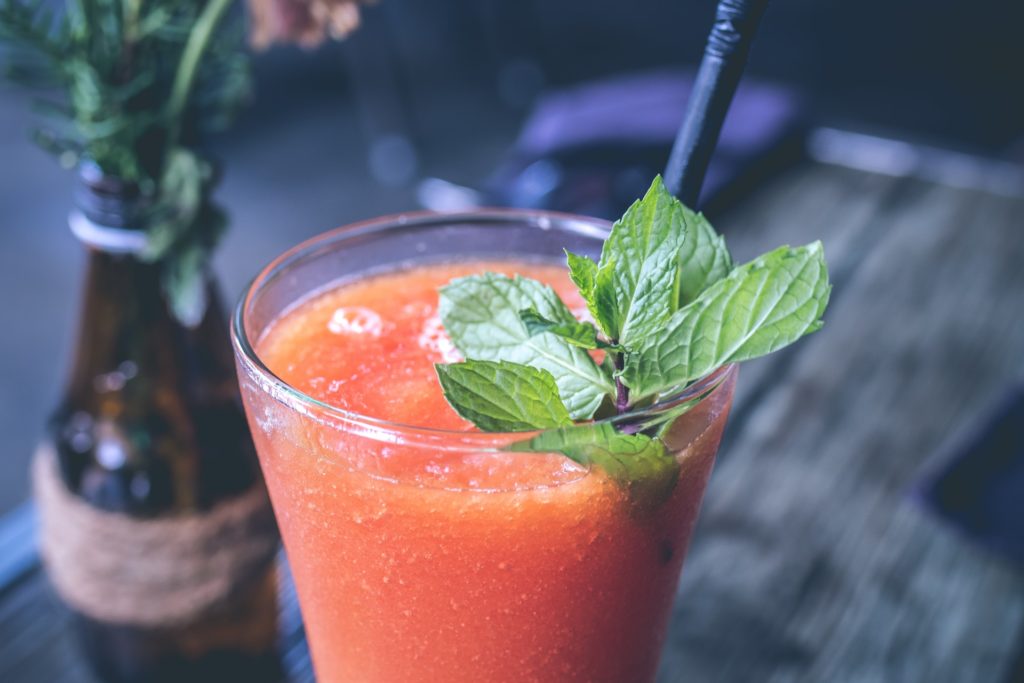 Crisp, cool, refreshing. Ah! Costa Rican Foods: An ice cold glass of carrot and orange juice is adorned with a black straw and green mint leaf. An old bottle filled with flowers sits adjacent.
