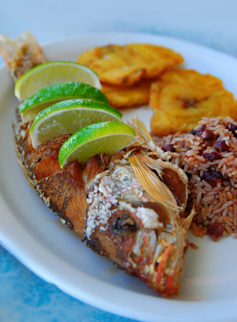 Lunch fresh from the sea! Costa Rican Foods Image: A serving of fried red snapper with pinto beans, rice, and tostones (Cuban plantains). Four lime wedges have been placed inside of slits made in the side of the fish.