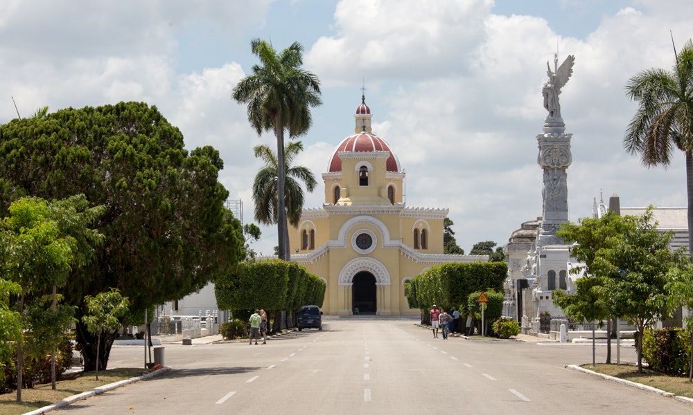 Quiet, sunny, and serene. Cuba Unusual Museum Image: A photograph of the cemetery; pale yellow with a red roof. The streets are lined with trees.