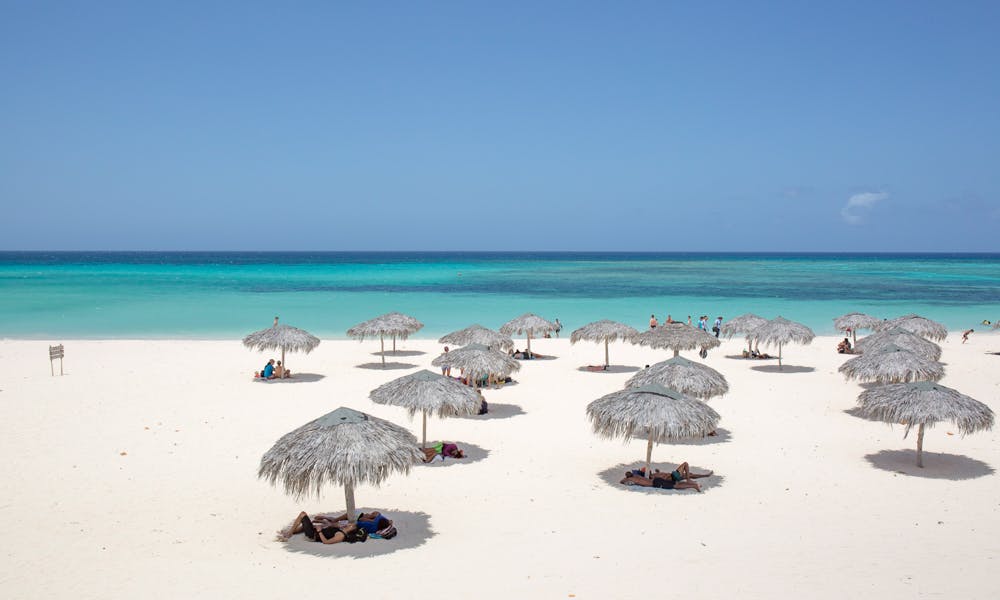 Exhale your stress, and proceed to indulge. Best Beaches Image: Cuba. A series of straw beach umbrellas creates circles of shade in the sand for beachgoers to cool off in. The sand is pristine, the water is inviting, and there is hardly a cloud in the sky.