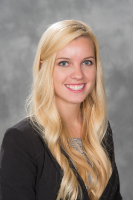 Sustainability Image: Kendall Scott has a big bright smile, vibrant blue eyes, and her blonde hair is draped over her dark jacket.