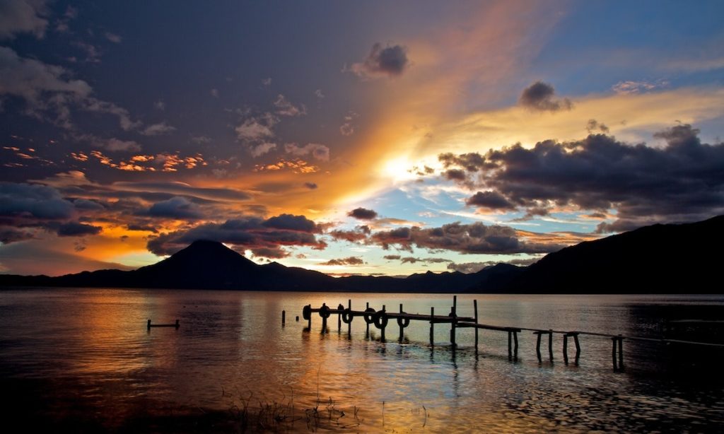 Has Lake Atitlán always been so beautiful? Mayan Image: A pier leading up to Guatemala's Lake Atitlán is caressed by a sun dappled sky in shades of blue, gold, and purple.