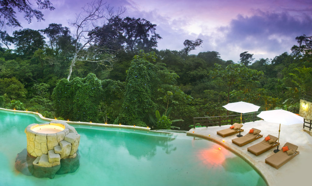 Hard to believe that this beautiful pool is actually a geothermal hot spring. Hot Springs Image: Hot Springs, Tizate. Beige lounge chairs and white umbrellas line a beautiful pool, which is in fact a hot spring. The background is a jungle and a purple sky.