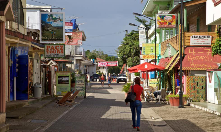 People watching and exploring city streets is one of life's simple pleasures. Belize and Guatemala Itinerary Image: A woman walks in denim and a red top carries a black shoulder bag as she walks down a colorful street in San Ignacio.