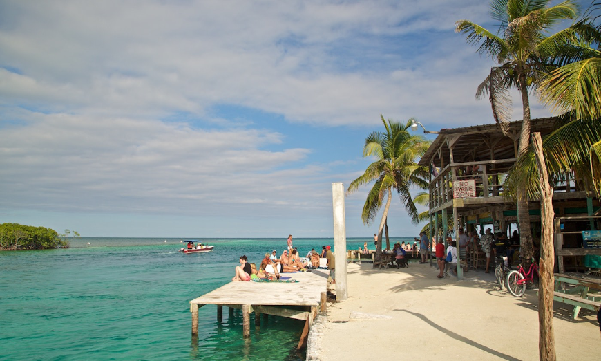Belize Island Image: People are milling about a snack bar and lounging on a pier, enjoying sunshine and turquoise waters.