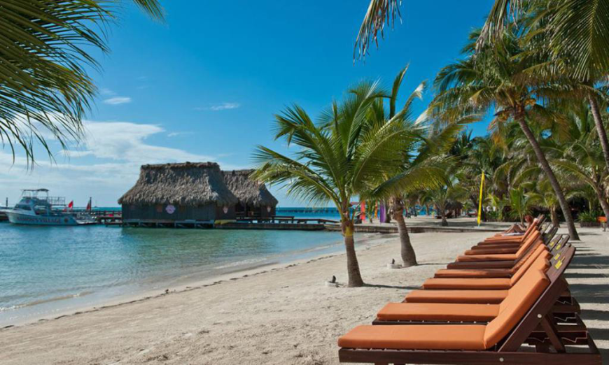Sit with a nice beach read and listen to the water lazily lap along the shore. Best Beaches for Swimming in Belize Image: A strip of Ramon's beach is dotted with a few palm trees. Wooden lounge chairs are in the foreground. Thatched roof bungalows are in the background.