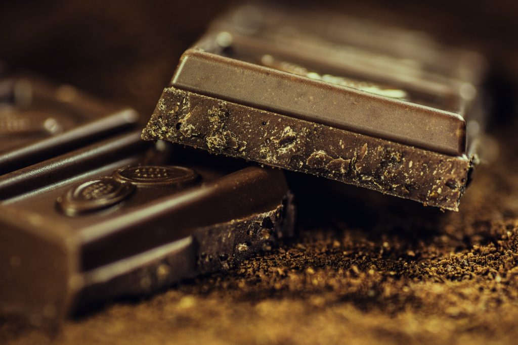 Have you ever stopped to appreciate just how beautiful high quality chocolate is? Best Chocolate Image: A close-up of a segmented chocolate bar broken, with one layer resting on top of another, and surrounded by coca powder and ground chocolate.
