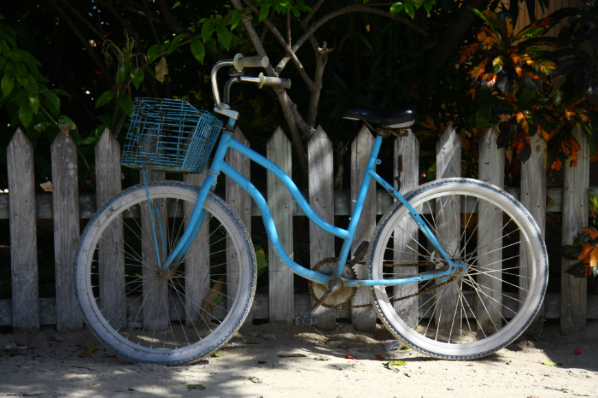 Best islands in Belize for Families Image: A cyan blue bike rests against an old white picket fence.