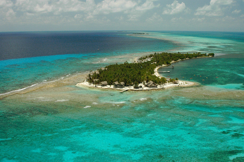 Blue seas and skies, green trees, and pristine sand. This is Belize at its finest. Best Surfing Beaches: An aerial view of Long Caye shows an abundance of green trees dappled with buildings along the shore.