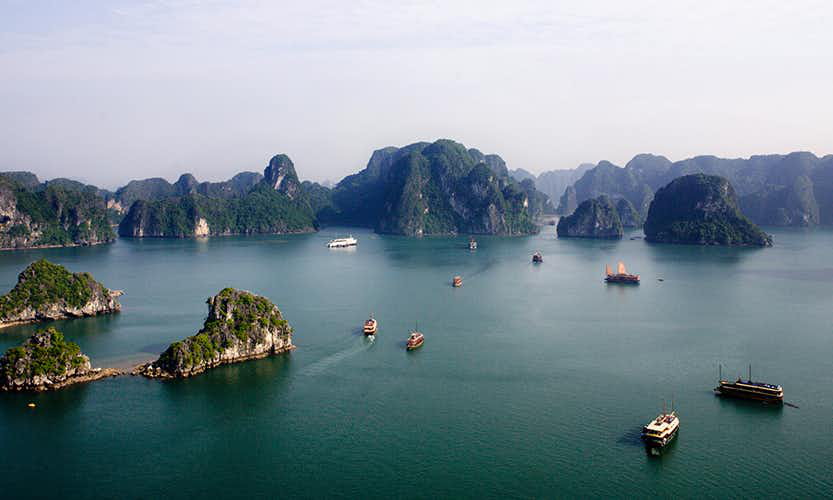 Sailing emerald waters just adds to the excitement of your adventures. Caving in Vietnam Image: Boats navigate the green mounds and waters of Ha Long Bay.