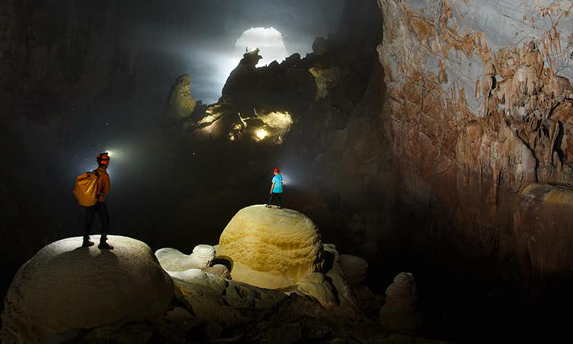 Become the explorer you've always wanted to be. Caving in Vietnam Image: Two people stand on large mounds in the massive Hang Son Doong cave.
