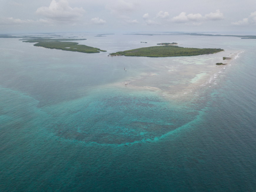 Notice how the water seems to glow... Central America Islands Image: An aerial of lush, green mounds of land, and coral that seems to glow peeking through water.