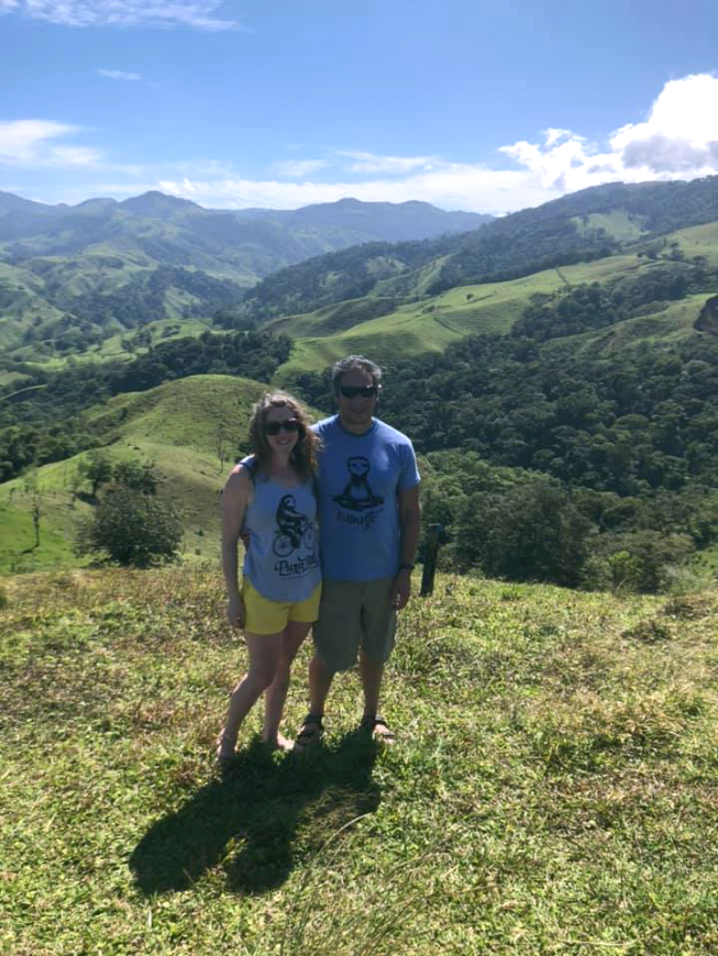 Costa Rica Couples Trip: The happy couple wears sunglasses while smiling on a sunny hillside.