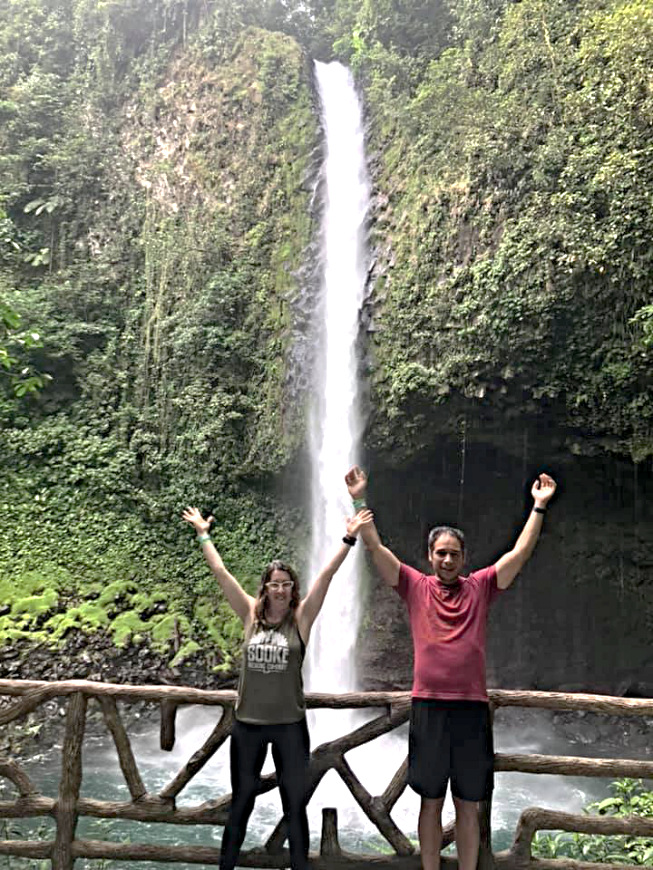Costa Rica Couples Trip: The Pearson/Lepine's smile with their arms over their heads in front of La Fortuna Waterfall.