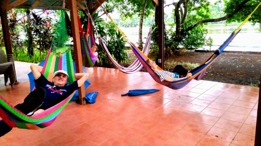Costa Rica Tortuga Lodge Image: Four people enjoy resting in colorful hammocks amongst lush scenery.