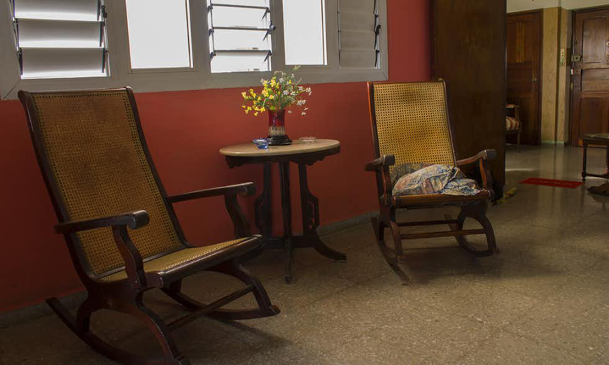 Cuban Homestays Image: Two rocking chairs on either side of a small table with vase of flowers near a window.