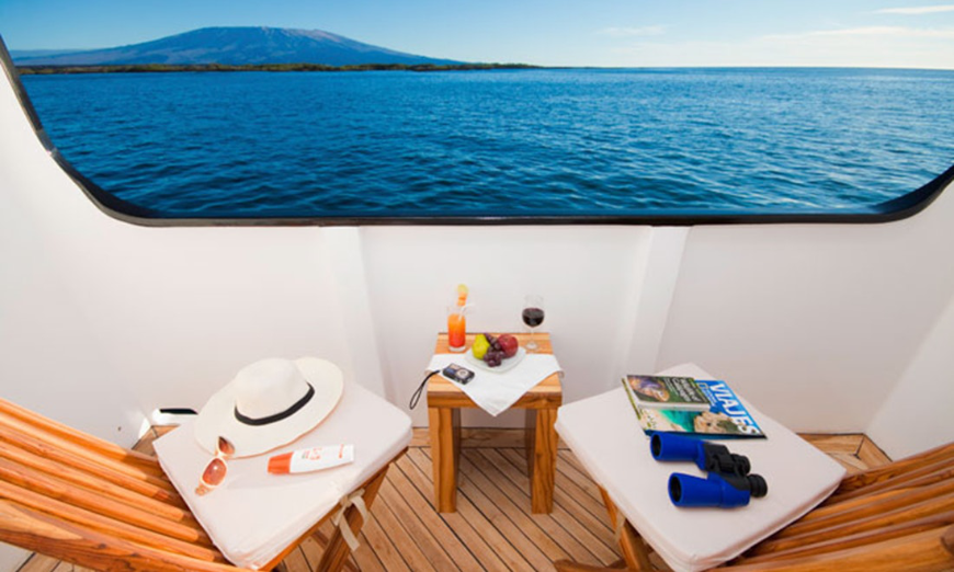 Adventure by day, luxury by night. Sounds like an ideal honeymoon... Destination Wedding in Ecuador Image: Magazine, binoculars, sunglasses, hat, sun cream, two chairs, and a table with drinks sit on a balcony overlooking the water mid cruise.