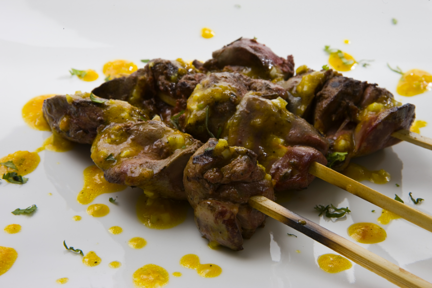 Why do some things seem to taste better when served on a skewer? Eat In Peru Image: Three anticuchos are on a white plate drizzled in a golden sauce.