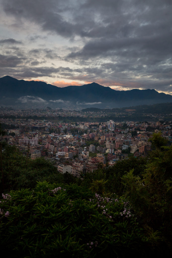 You will see many amazing views on your trek to Everest Base Camp. Everest Base Camp Image: A view of the city of Kathmandu, Nepal as seen from the wilderness with mountains seen in the background, peeking from a low-lit sky.