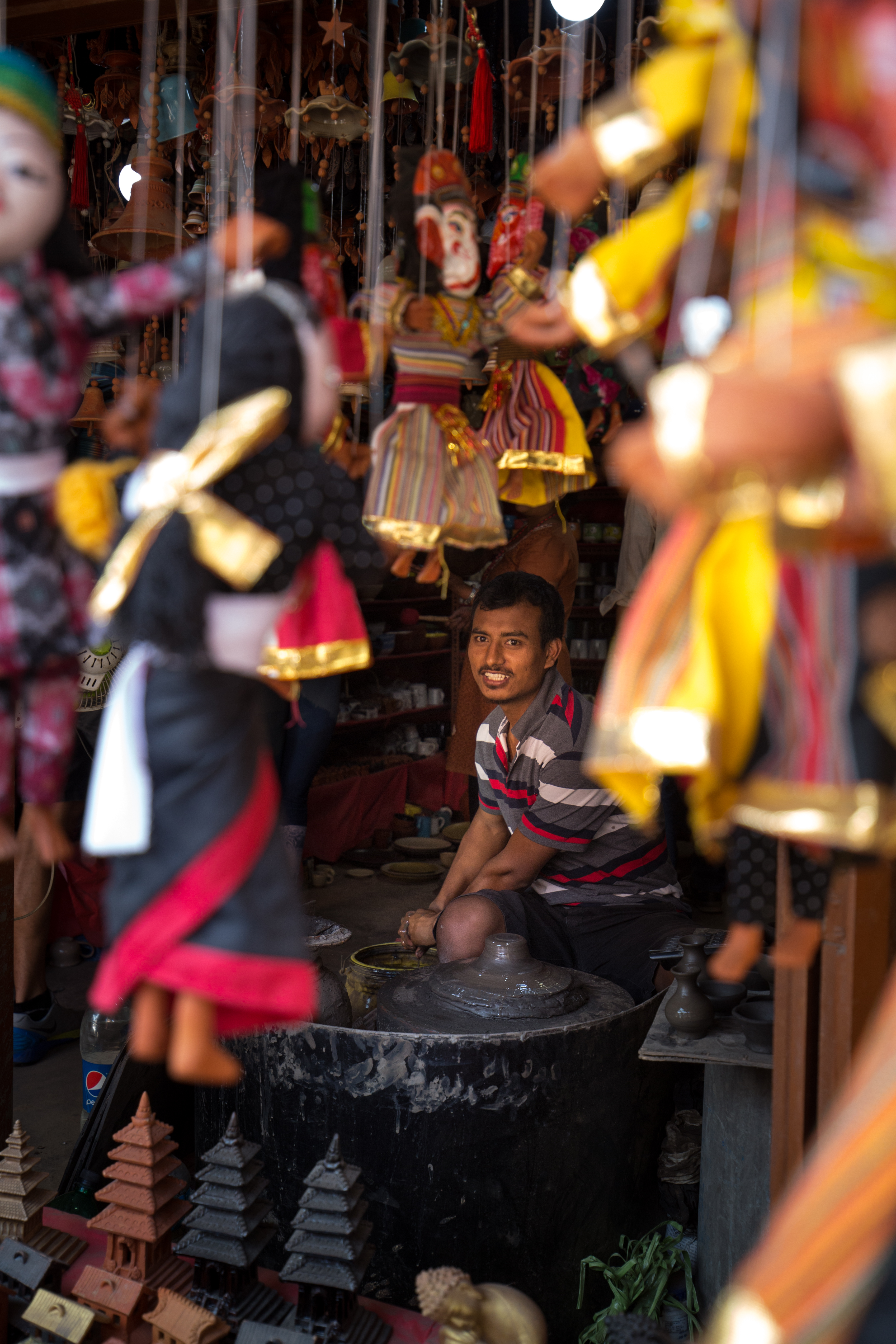 It's okay to bring back more than memories. These handmade items would make lovely souvenirs. Everest Base Camp Image: An artisan is seen gently smiling from behind a barrage of multicolored puppets suspended from strings, a pottery wheel, and small statues.