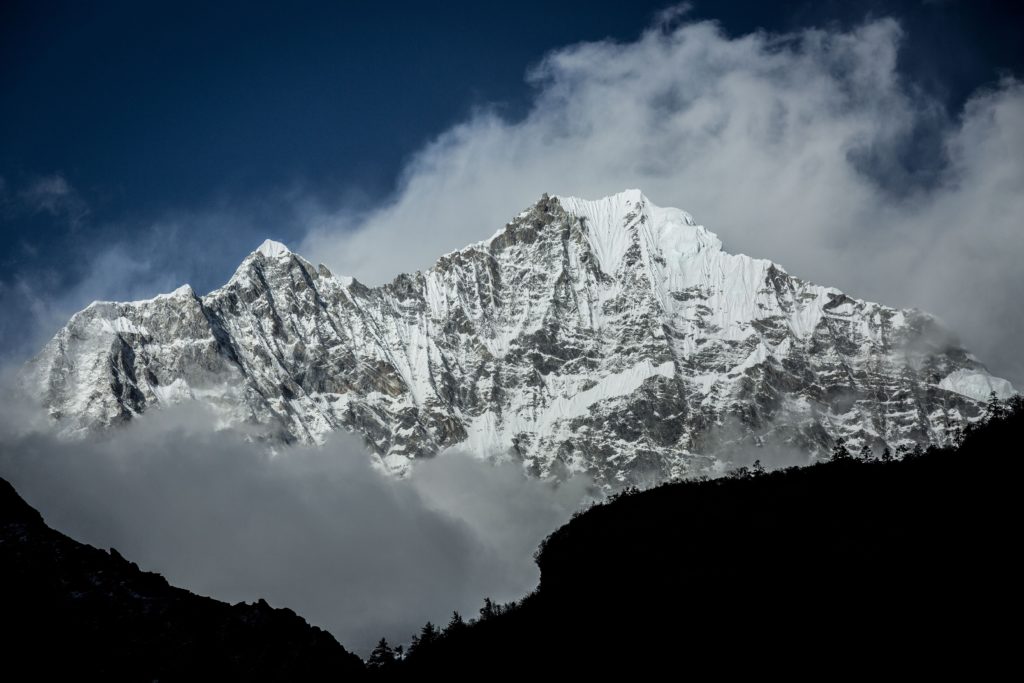 A Mount Everest graced in a dusting of snow emerges from mist, swirling up into a cloudless blue sky.