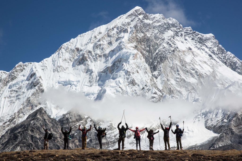 You'll celebrate too when you go on this excursion. The Everest Base Camp trek team strikes a pose in front of the namesake mountain. The photo is taken at a distance, so it is difficult to make out their individual faces.