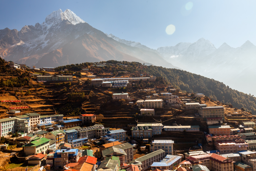 Looming mountains are beautifully inescapable. Everest Tattoo Image: Mountains loom over the buildings of Namche Bazaar — shown at a distance.
