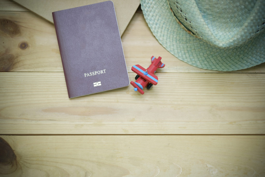 You can't just grab your passport and go, but with a little planning, your next family holiday can be a great adventure. Family Adventure Image: On a wooden floor sits a passport, mint green straw hat, and a red toy plane with blue stripes.