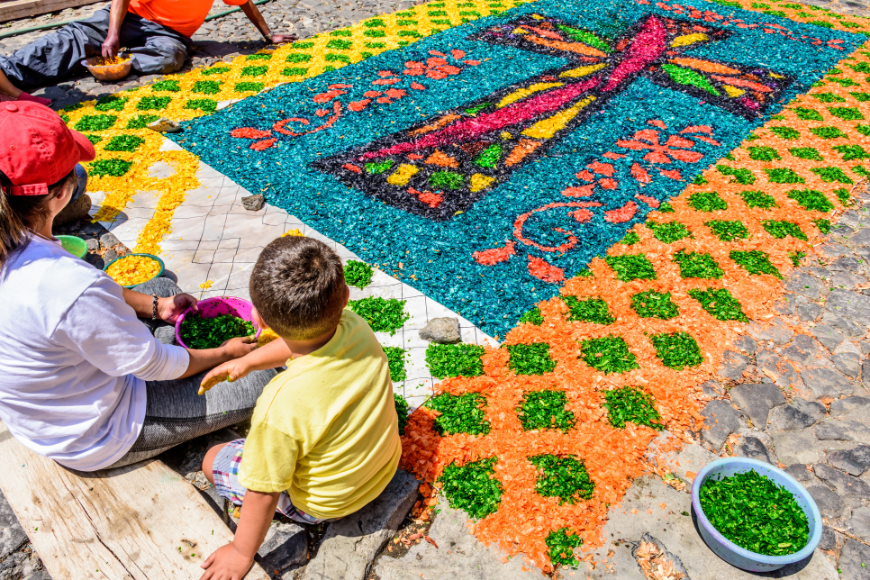 Don't just observe local customs on your holiday — join in! (When appropriate.) family vacations in belize and guatemala image: A family works on a holy carpet using colored sawdust.