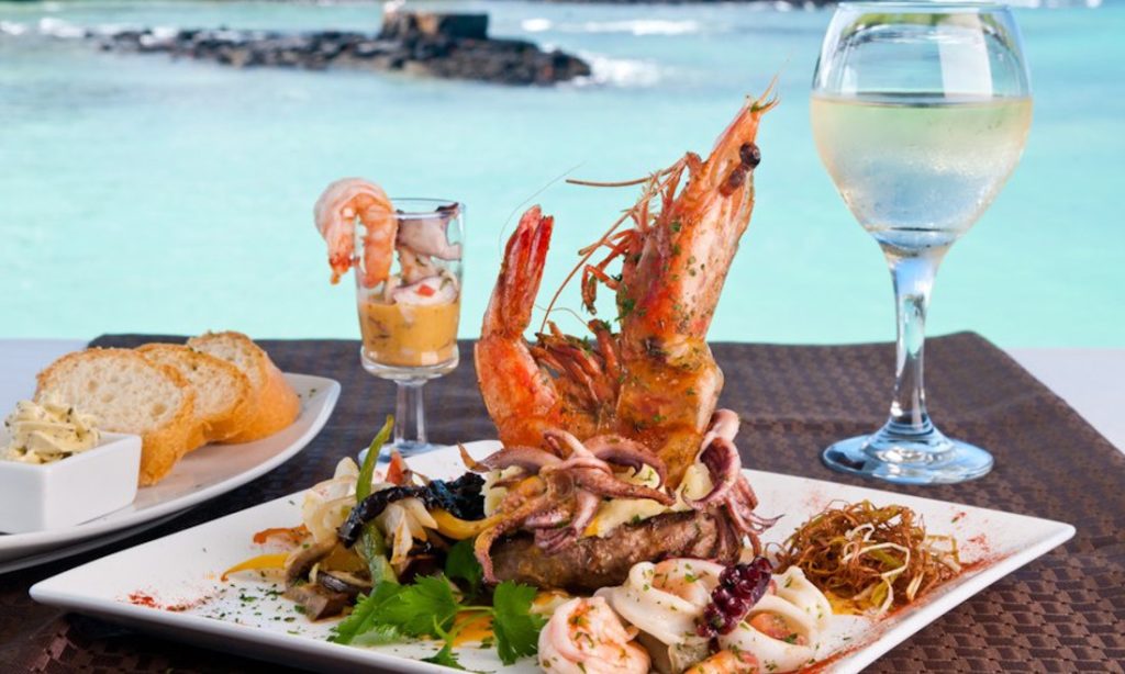 Beautiful scenery, beautiful meal. #BestHolidayEver Galápagos Islands Image: A beautiful seafood based meal shows a positioned giant prawn and other delights on a table with an ocean view in the background.