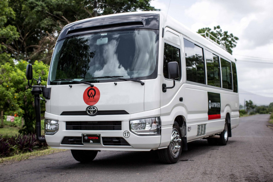 Getting Around in Costa Rica Image: A white Anywhere shuttle drives down a tree-lined road.