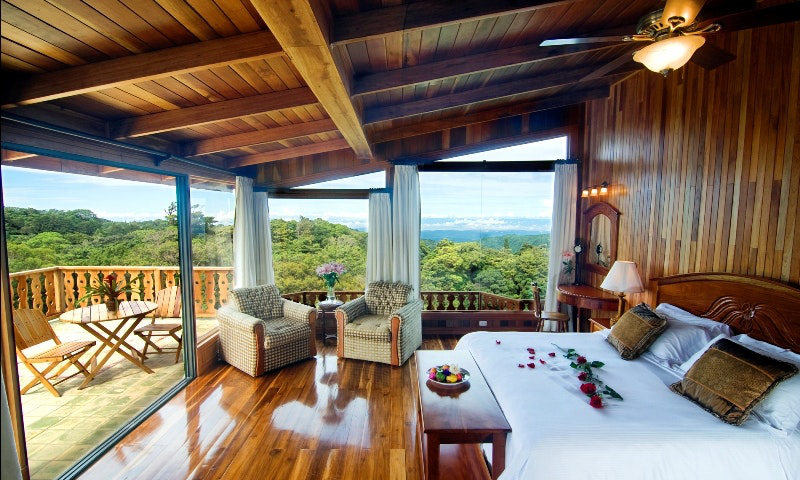 Luxury for less is real during the off-season. Green Season Image: A rose covered bed and balcony with bistro set and view at Belmar Hotel.