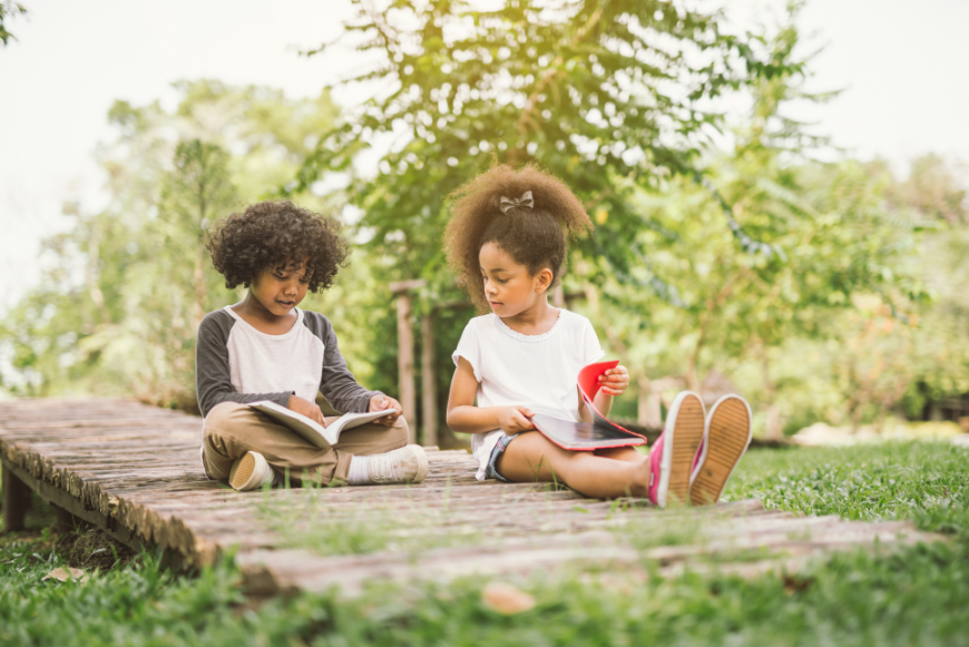 Why play video games when you can read a great book in the Costa Rican sunshine? Imagination Bus Image: Two children with curly hair sit and enjoy books outside.