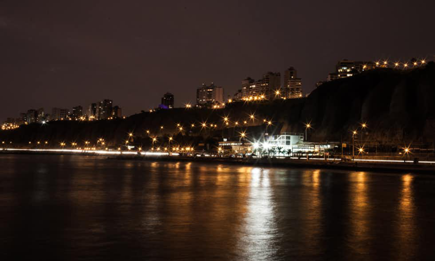 Discover the beauty and fun of Lima at night. Lima Nightlife Image: View of the city from the coastline, lit up at night.