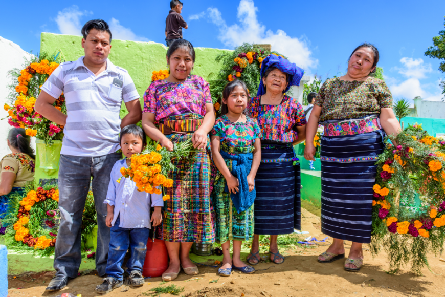Family members don't cease to be family just because they are no longer on this plane. Mayans of Guatemala Image: A family of six (mother, father, son, daughter, aunt, and grandmother) wear bold clothes, hold vibrant flowers, and pose in a colorful Guatemalan cemetry.