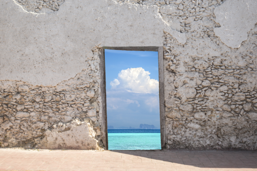 A tropical island is one door; yours may lead to a cosmopolitan city. Moving Abroad Image: A weathered wall has a doorway cut into it, leading to a blue sea and sky.