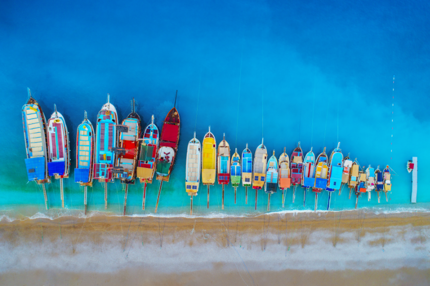Next stop: BELIZE! Moving Abroad Image: Colorful boats sit in vibrant blue water along a sandy shore.